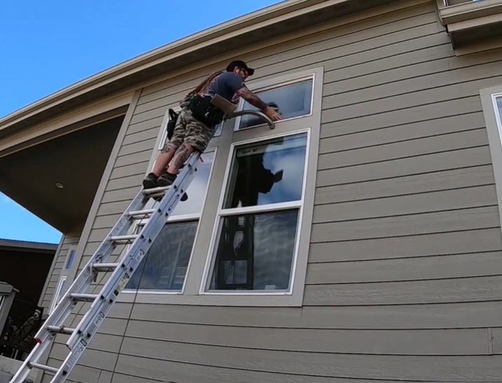 Residential window cleaner on ladder cleaning second-story window on a San Clemente home
